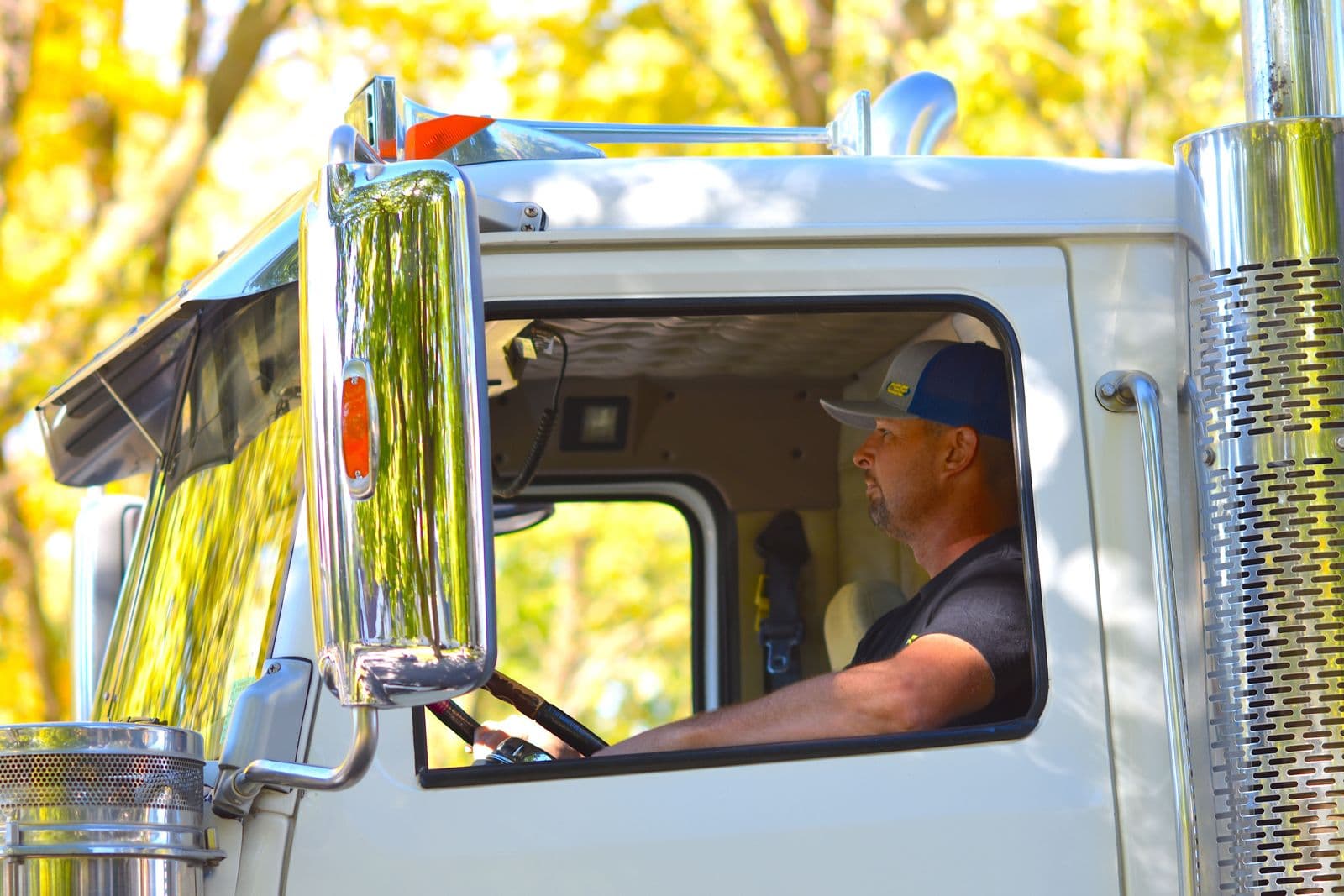 A truck driver in a large commercial vehicle driving through a sunny landscape.